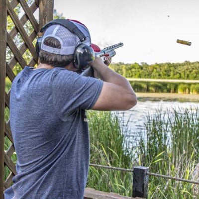 shooter shooting shotgun outside near a pond