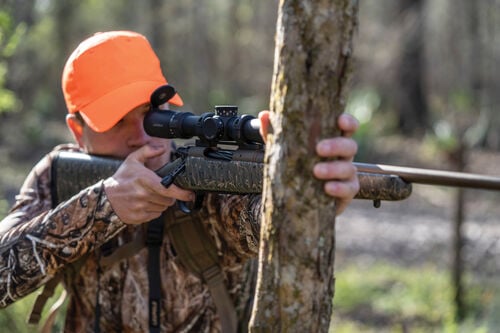 man shooting rifle from a tree stand
