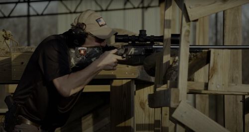 Jim Gilliland looking down a scope of a rifle rested on a wooden stand