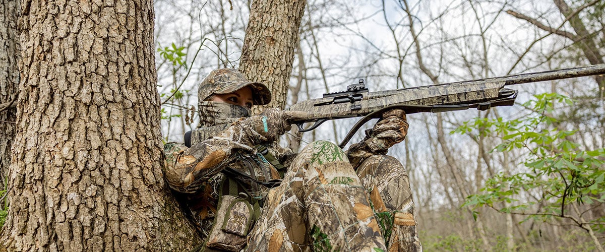Hunter aiming a shotgun next to a tree