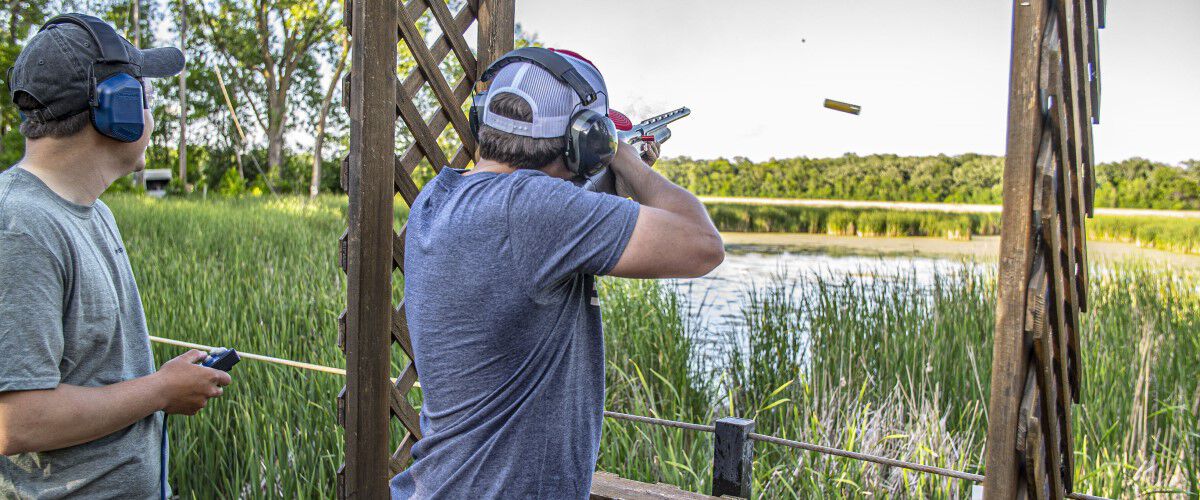shooter shooting a shotgun outside near a pond