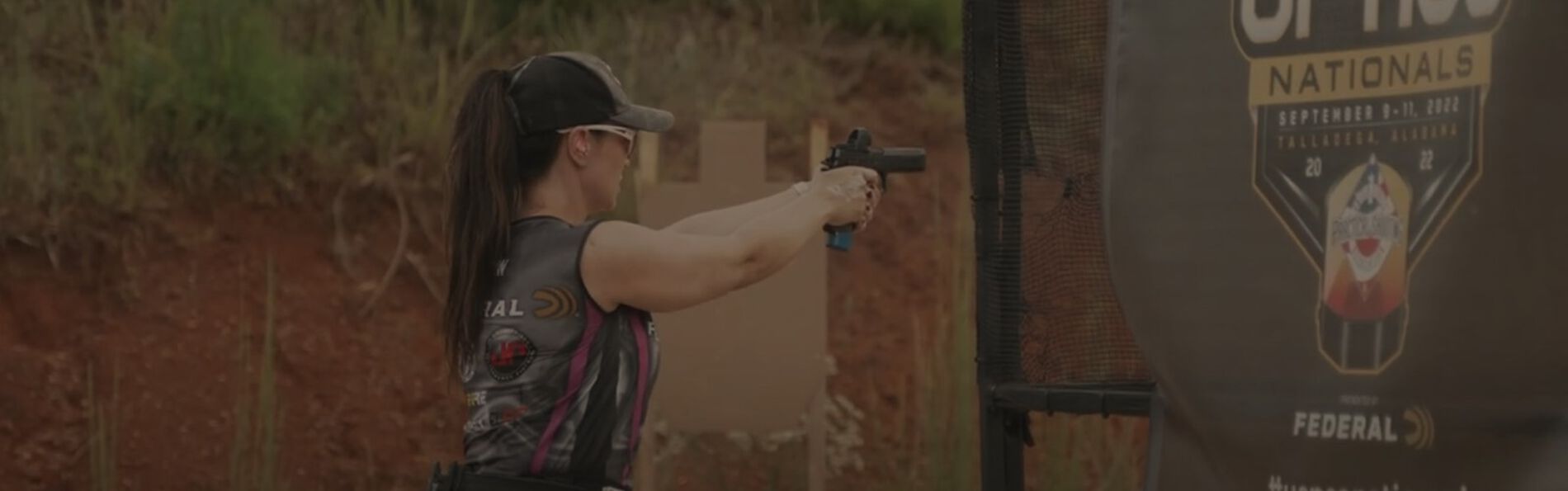 Krystal aiming his pistol with a red dot attachment at a competition