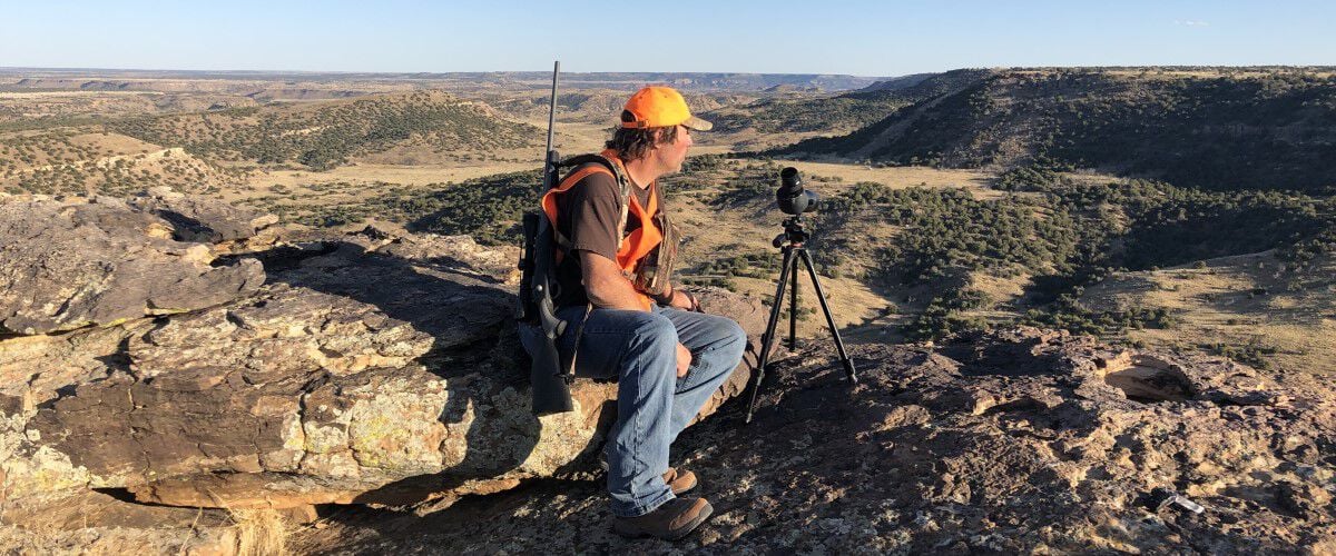 Hunter sitting near a cliff with a range finder looking for deer on the prairie