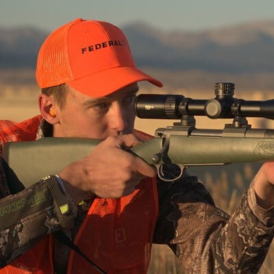 Two hunters hiding in the grass aiming their shotguns