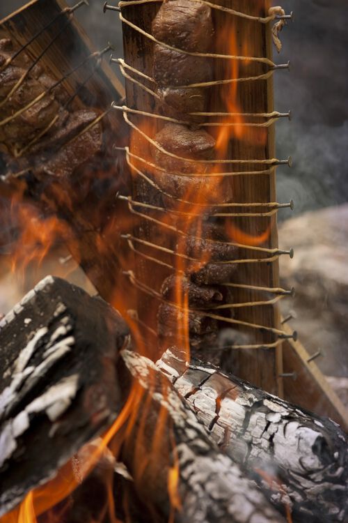 Steak tied to a plank cooking on an open fire