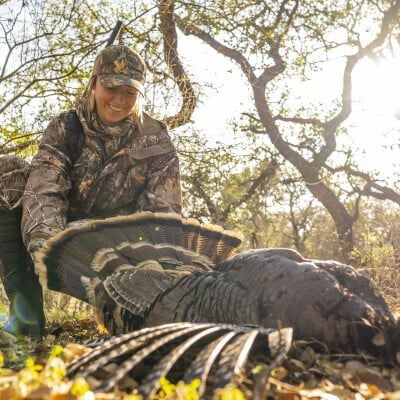 hunter behind a dead turkey laying on the ground
