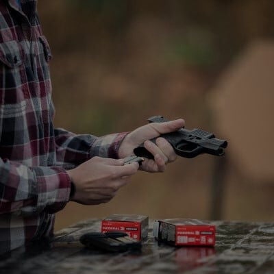 Hangun magazine being loaded into a handgun with Federal ammo on a table