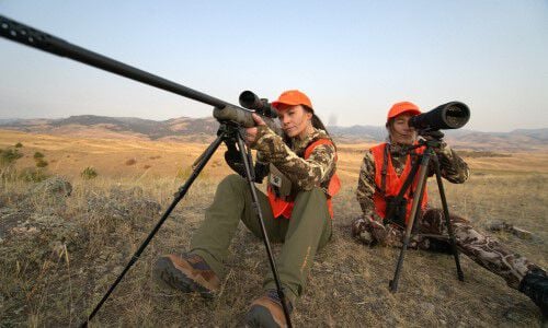 one woman looking down a rifle scope and another woman looking down a range scope