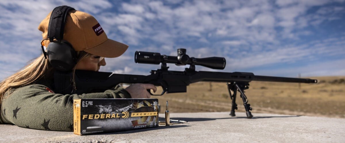 shooter looking through a rifle scope with a box of Terminal Ascent on a table