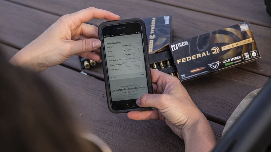 person looking at the federal app on their phone with boxes of Gold Medal Sierra MatchKing in the background