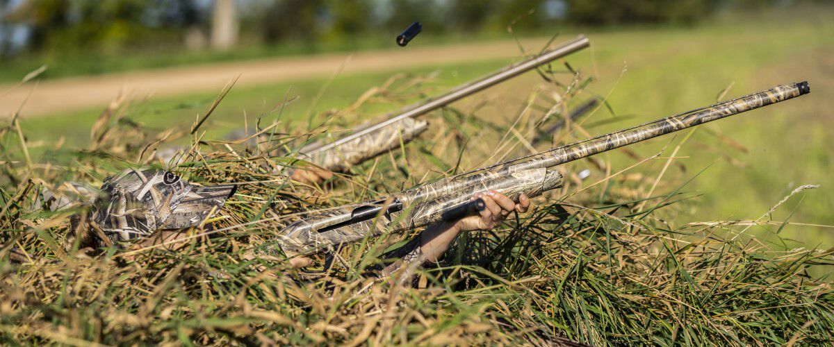 hunters hiding in a duck blind with their shotguns aimed