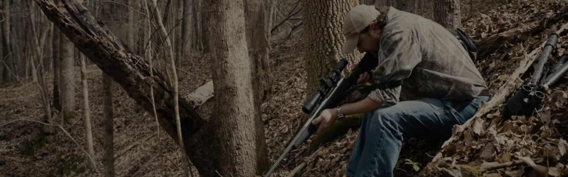 Jim Gilliland using a sling and aiming his rifle on a slope covered in leaves