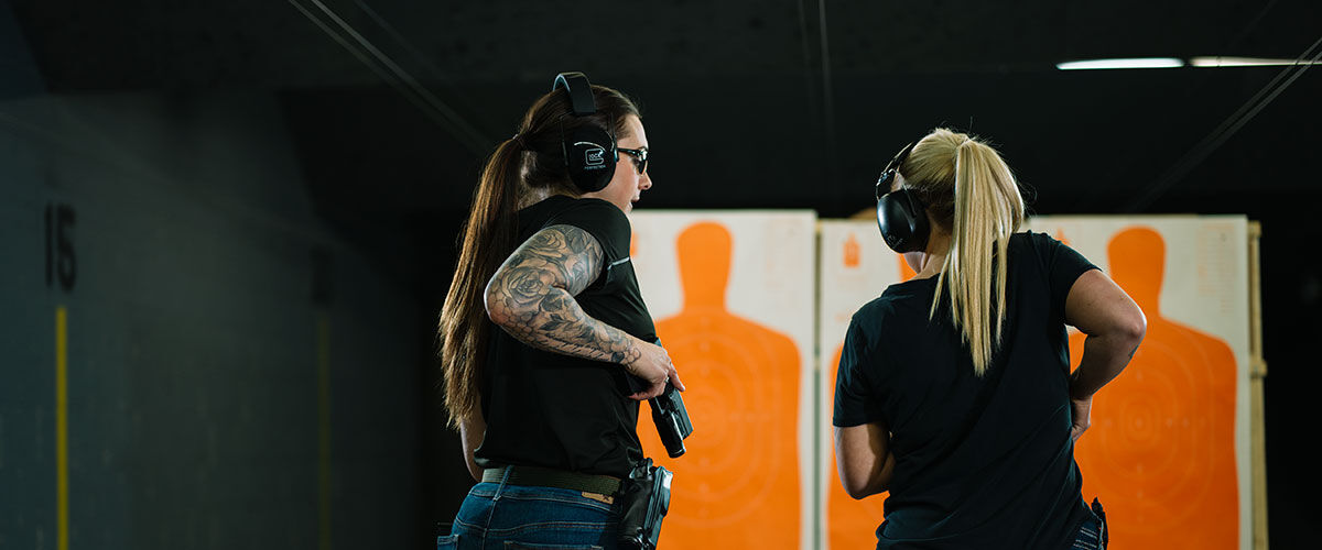 One person watching another shoot a handgun at an indoor gun range