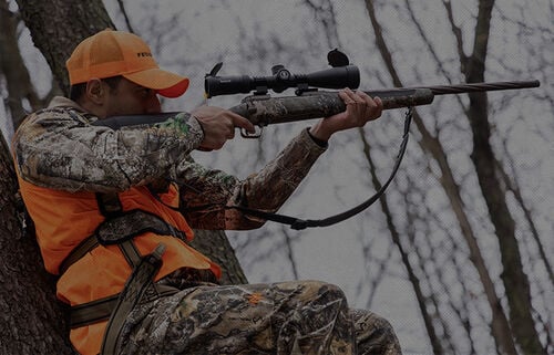 man shooting rifle from a tree stand