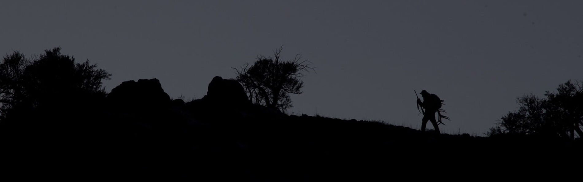 silohetted Hunter walking up a hill with antlers in his backpack