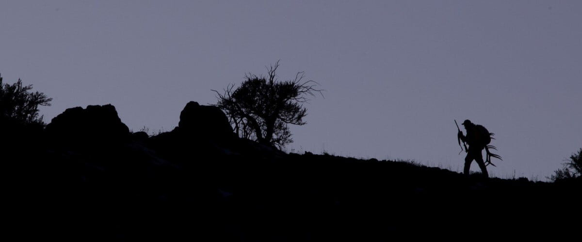 silohette hunter carrying horns while walking up a hill