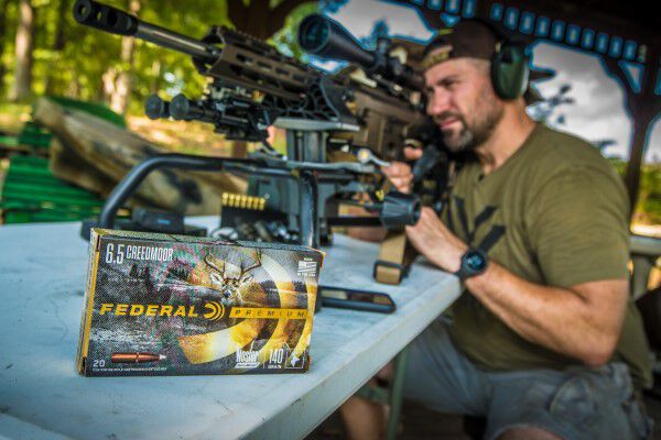 Kip Campbell looking down a rifle scope with a box of Federal Premium Nosler Accubond beside him