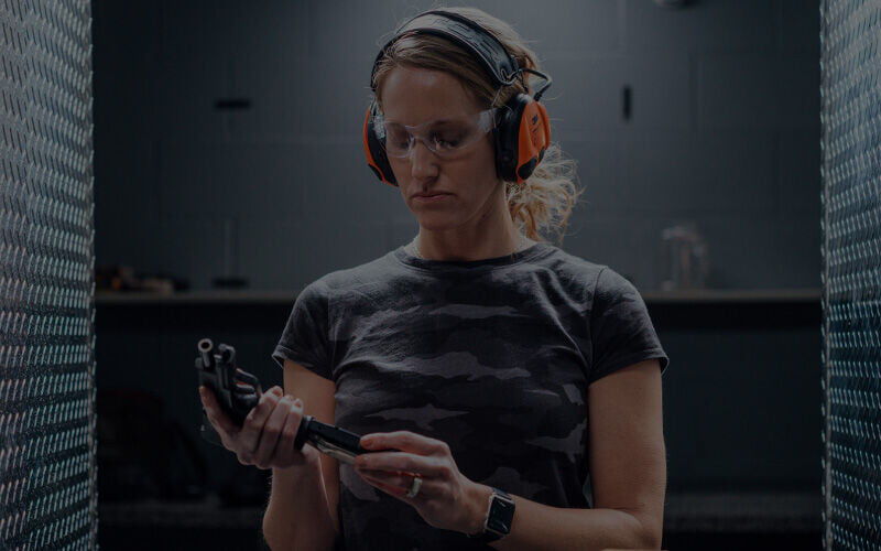 female shooter loading a pistol at an indoor range