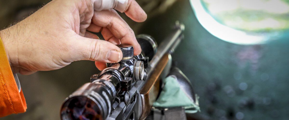 person adjusting a rifle scope dial