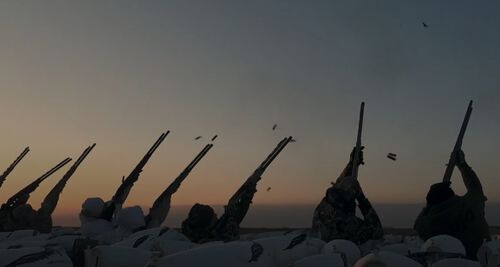 a group of hunters in a field aiming their shotguns at passing snow geese