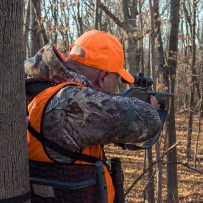 hunter aiming rifle while in a deer stand