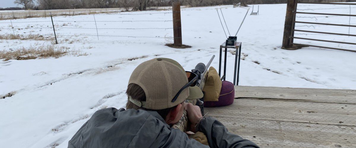 man aiming rifle while outside in the snow