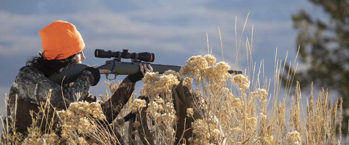 female hunter looking down a rifle scope on the top of a hill