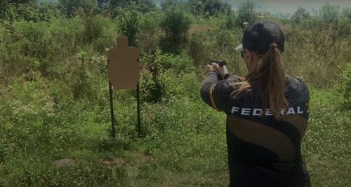 Julie Golob pointing a pistol at a target outside