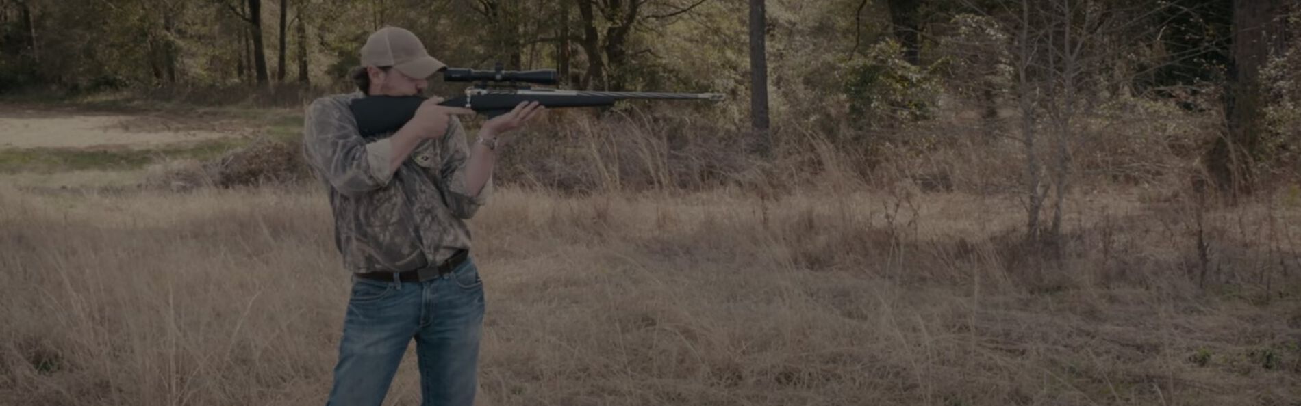 Jim Gilliland standing and aiming a rifle outside