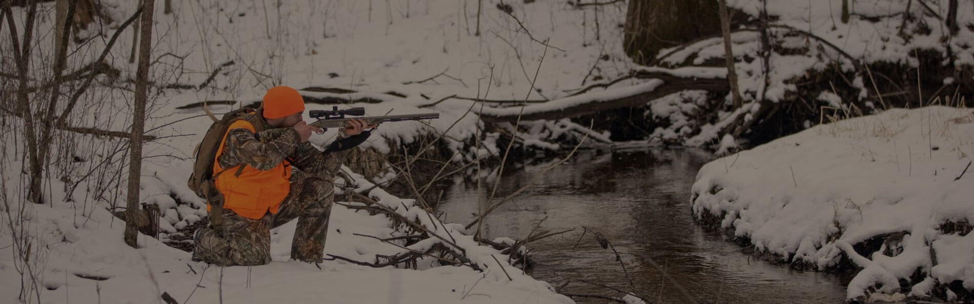 hunter kneeling in the snow while aiming a rifle
