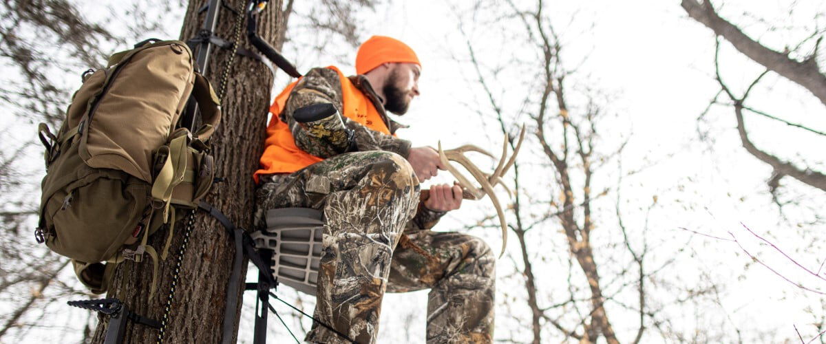 hunter sitting in a tree stand calling in deer with antler