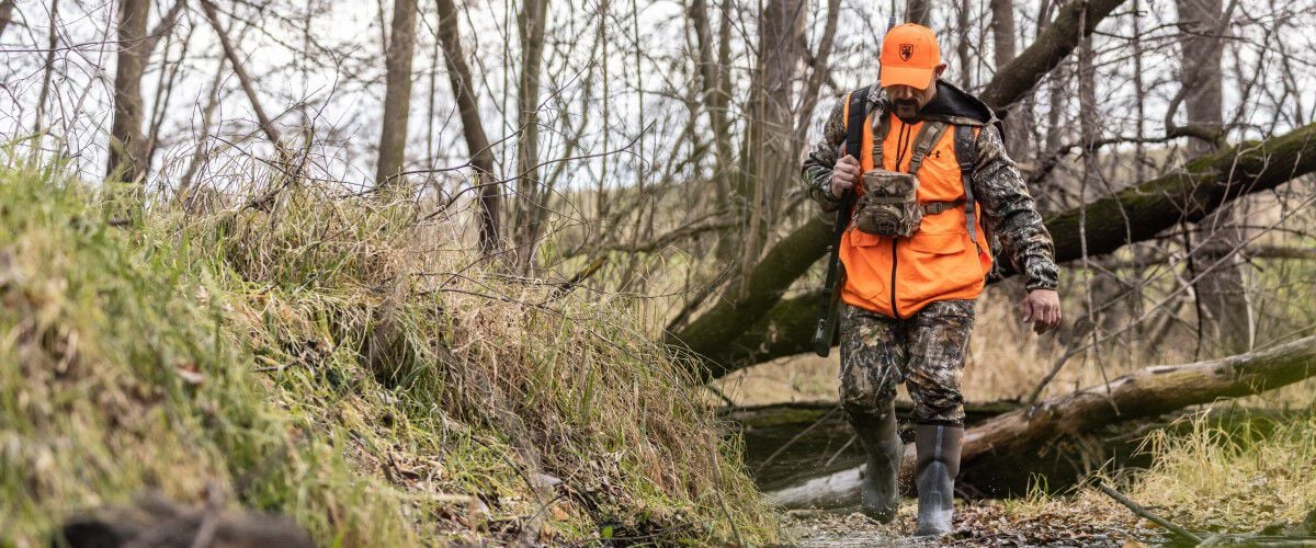 hunter walking through a wooded area with his rifle on his back