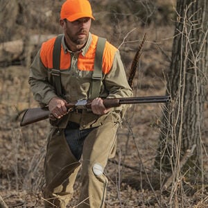 hunter walking in a wooden area carrying a shotgun and wearing Federal X Duluth Pack vest and chaps