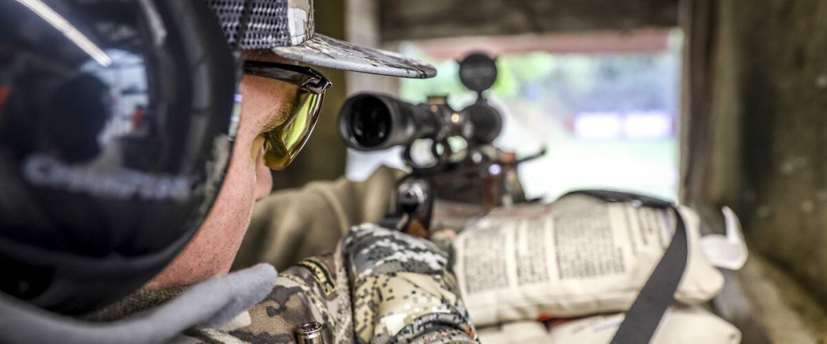 man looking down rifle scope at outdoor range
