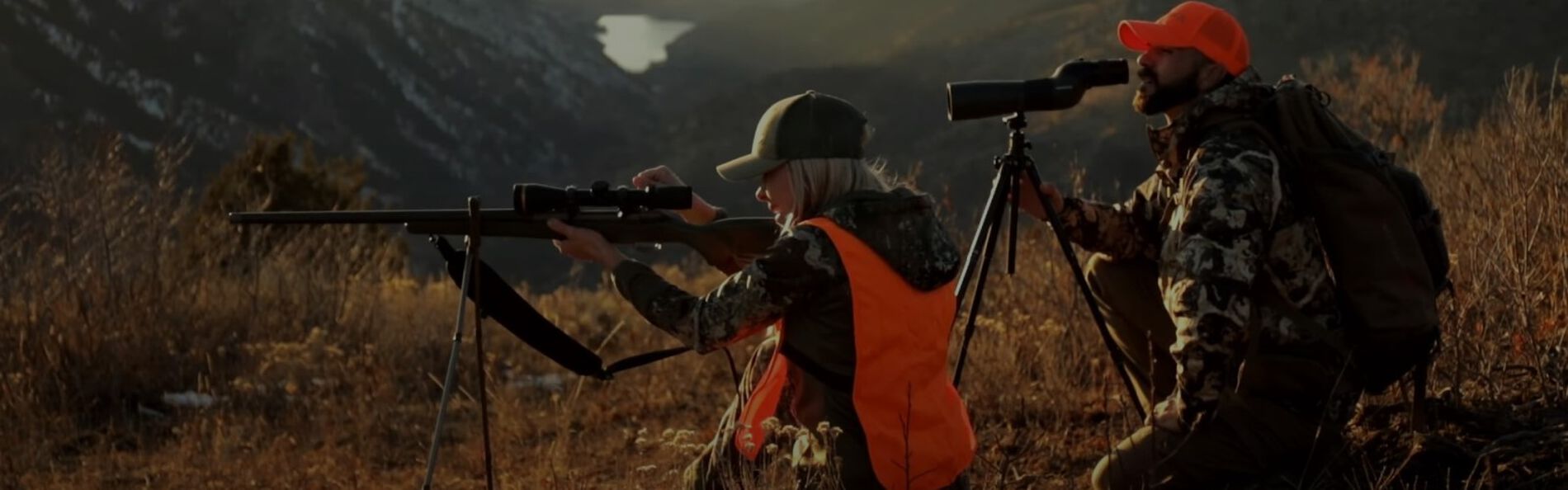 male hunter looking through spotting scope and female hunter looking down a rifle scope