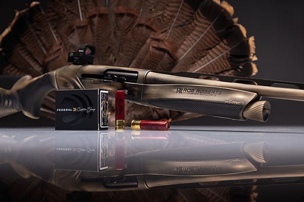 Robert Roberts custom shotshells and box in front of a shotgun and turkey tail 