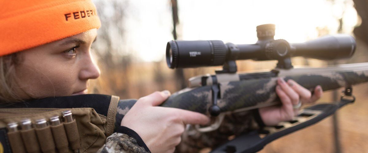 female hunter looking down the scope of her rifle