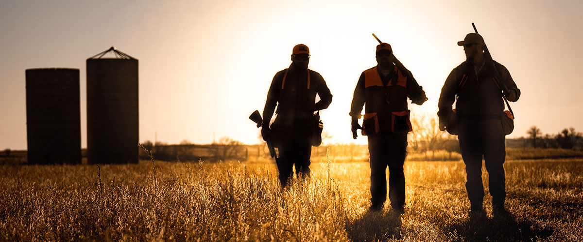 3 hunters walking in a field at sunrise