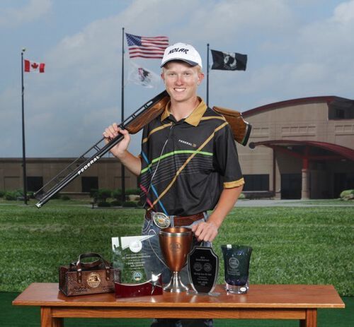Grayson Stuart with his shotgun standing in front of a trophy