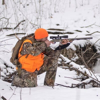 hunter kneeling in the snow while aiming a rifle