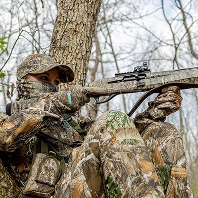Hunter aiming shotgun next to a tree