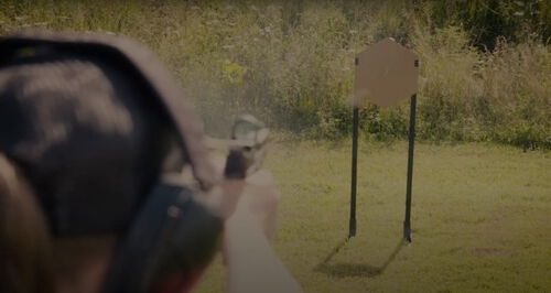 Julie Golob aiming a handgun at a wooden target