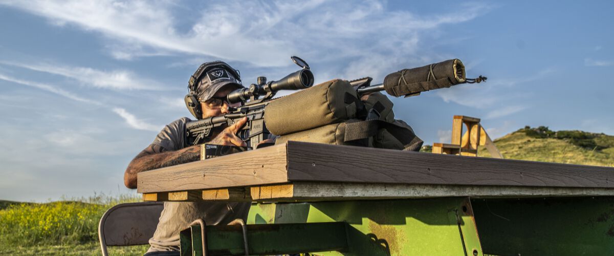 man looking down the scope of a rifle resting on a table