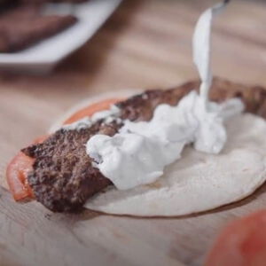venison gyros being topped with cucember sauce