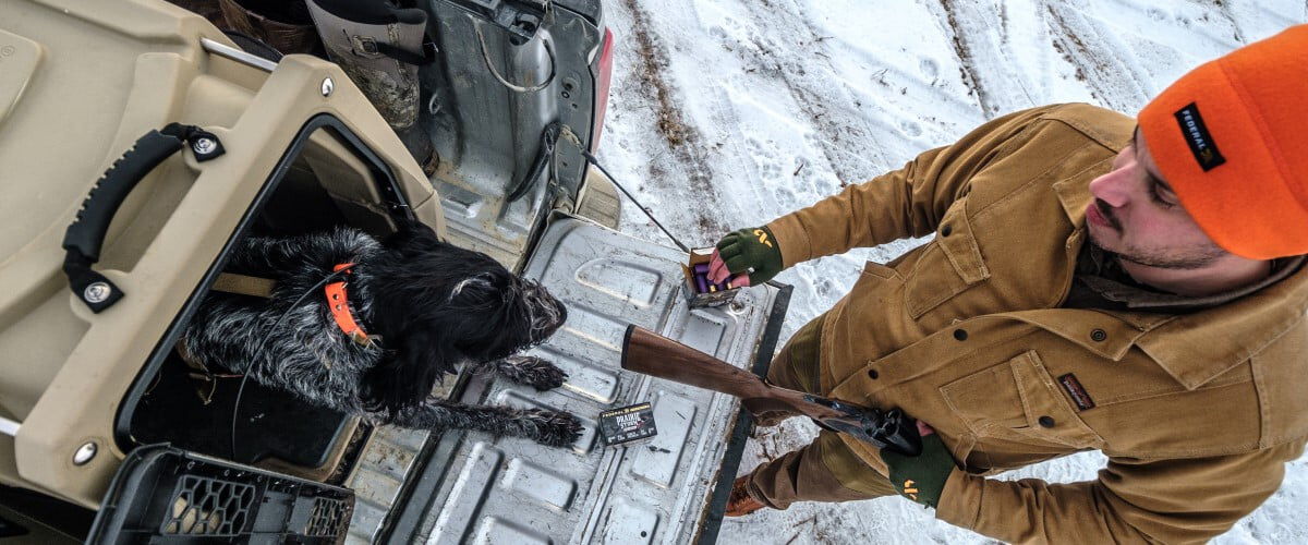 hunter standing in the snow next to a tailgate with his dog