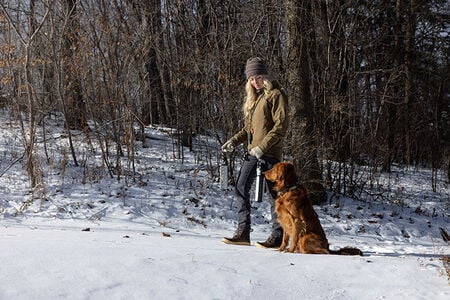 female wearing Cirque jacket standing in the snow with a hunting dog