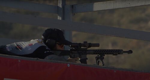 Josh Froelich looking down the scope of a rifle while laying down