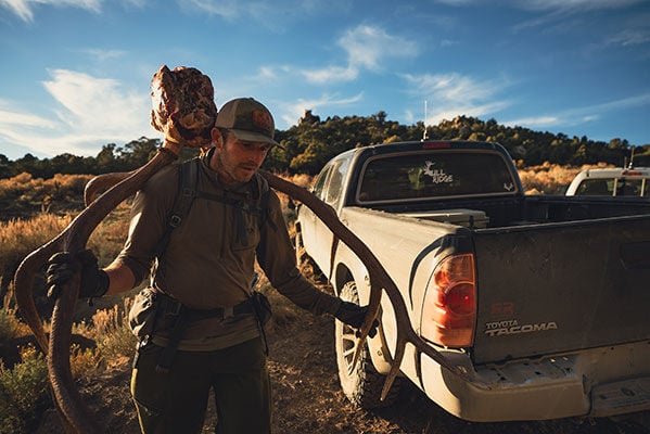 hunter carrying elk skull on his back next to a truck