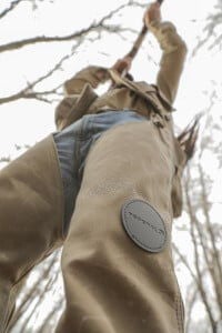 upward angle of hunter wearing chaps and aiming shotgun