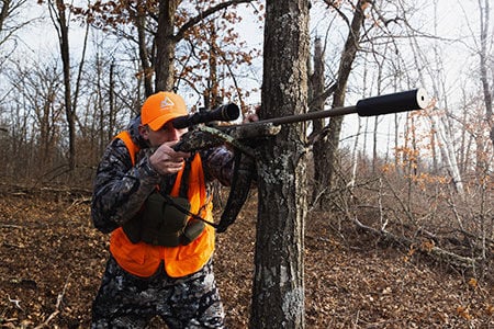 hunter resting rifle against a tree while aiming